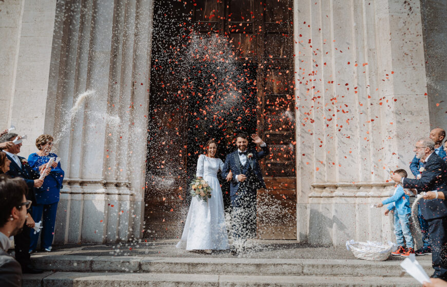 due sposi escono dalla chiesa mentre gli invitati tirano loro riso e petali