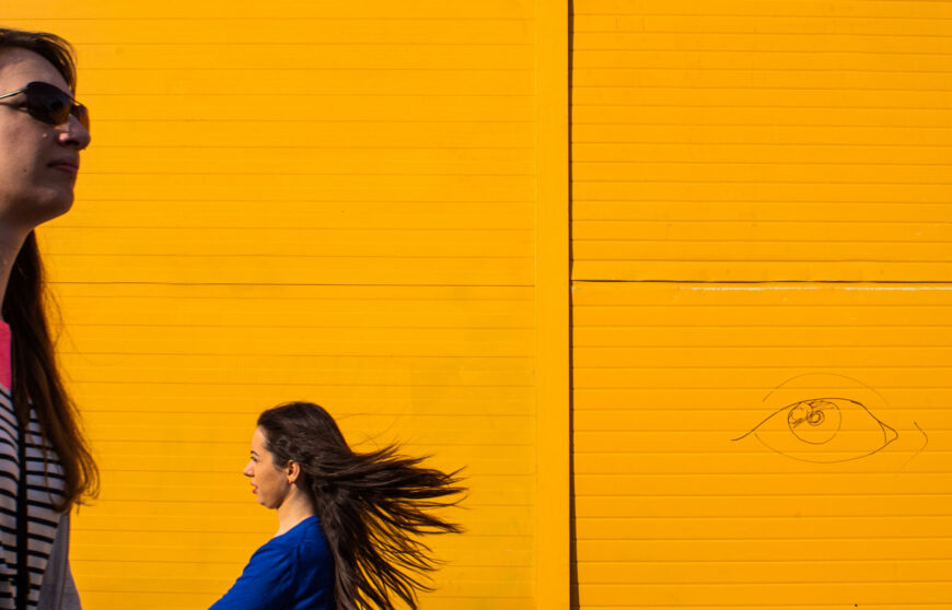 people walking in front of a yellow wall