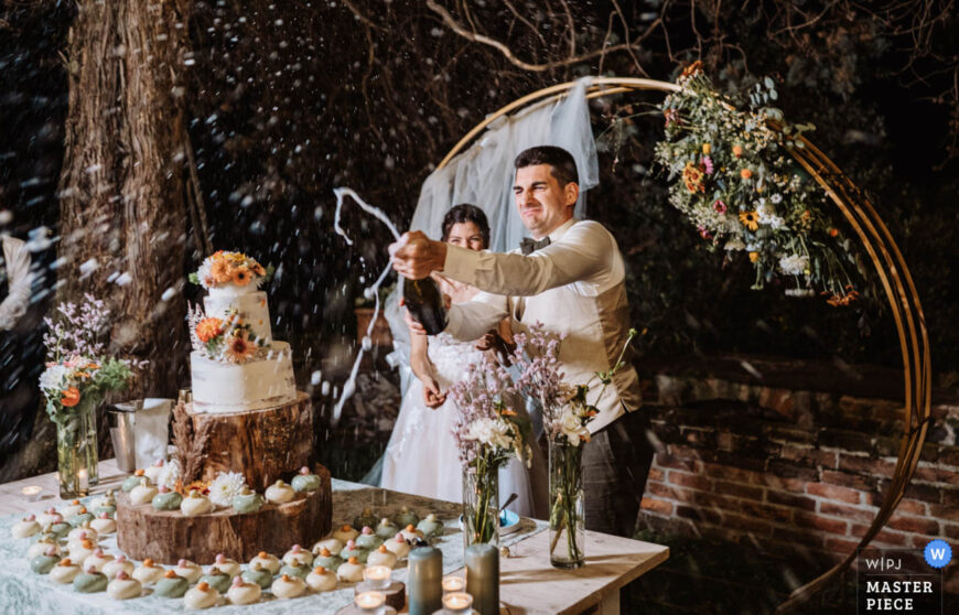 uno sposo stappa lo spumante e schizza gli invitati durante il taglio della torta di un matrimonio